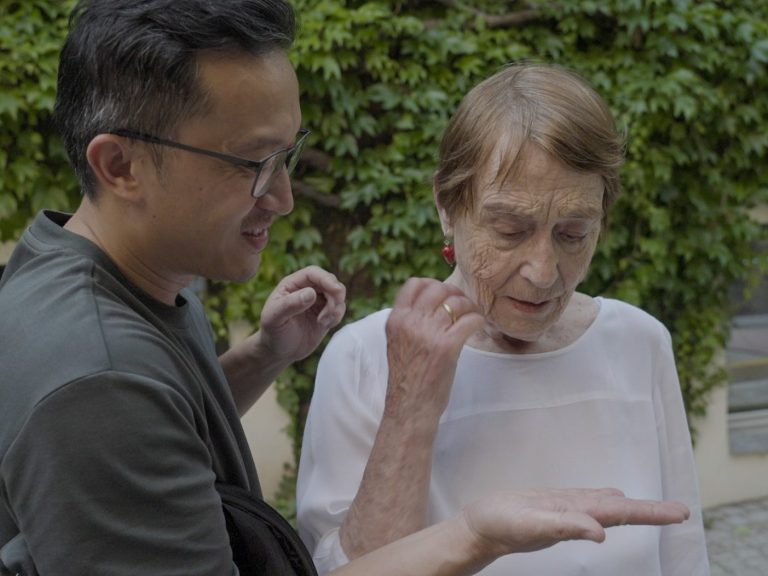 Regisseur Martin Nguyen mit Brille zeigt in seiner Handfläche Renate Welsh etwas