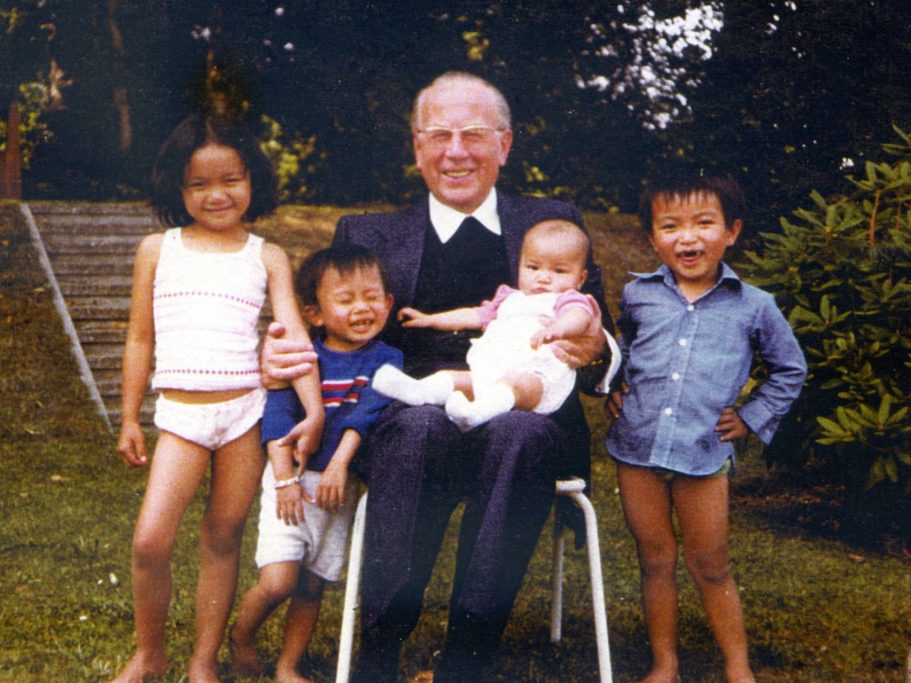 Kardinal König sitzt auf einem weißen Gartenstuhl, drei kleine vietnamesische Kinder stehen um ihn herum, ein Baby sitzt auf seinem Schoß